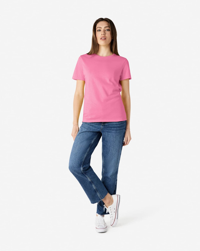 A pink Gildan Heavy Cotton Ladies' T-Shirt worn by a model paired with blue jeans and white sneakers.
