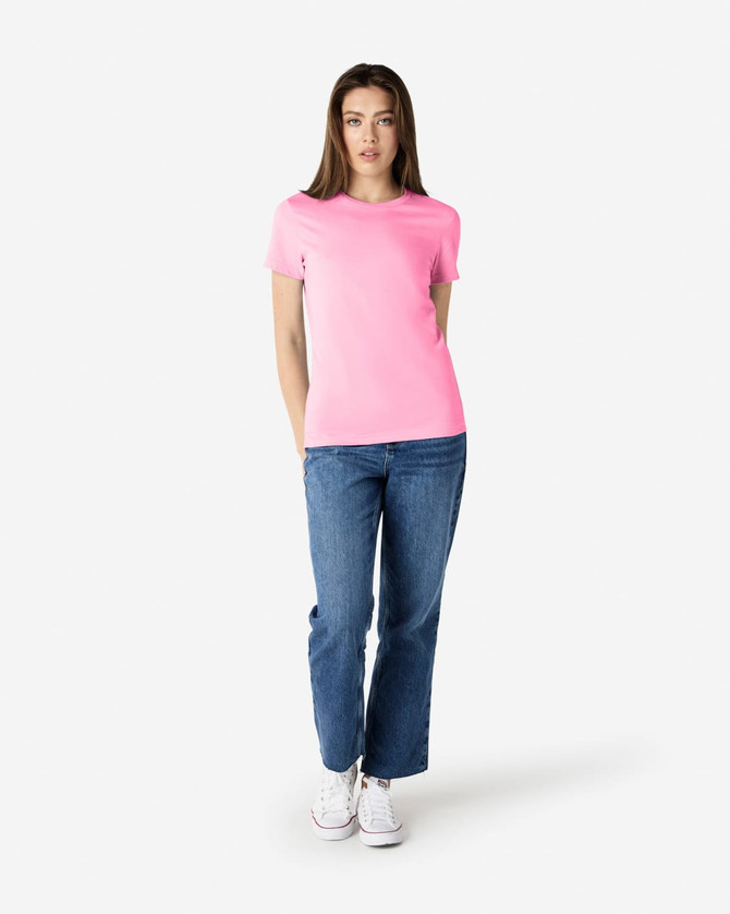 A pink Gildan Softstyle ladies' t-shirt paired with blue jeans and white sneakers, featuring a logo.