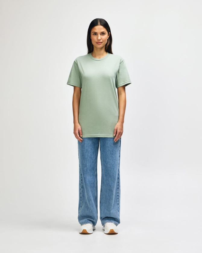 An olive green midweight t-shirt worn by a model, paired with black jeans and sneakers, featuring a logo.