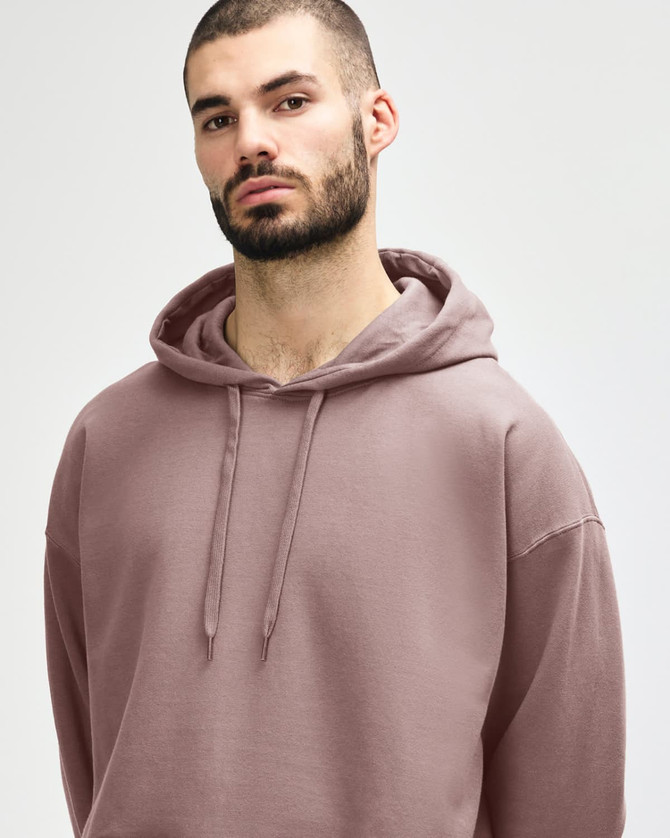A woman wearing a pink Gildan Softstyle adult hooded sweatshirt, with her hands near the hood.