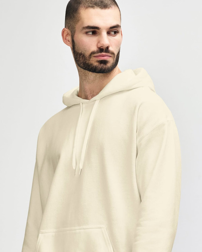A man wearing a cream-coloured Gildan Softstyle adult hooded sweatshirt, styled with denim jeans and a relaxed pose.