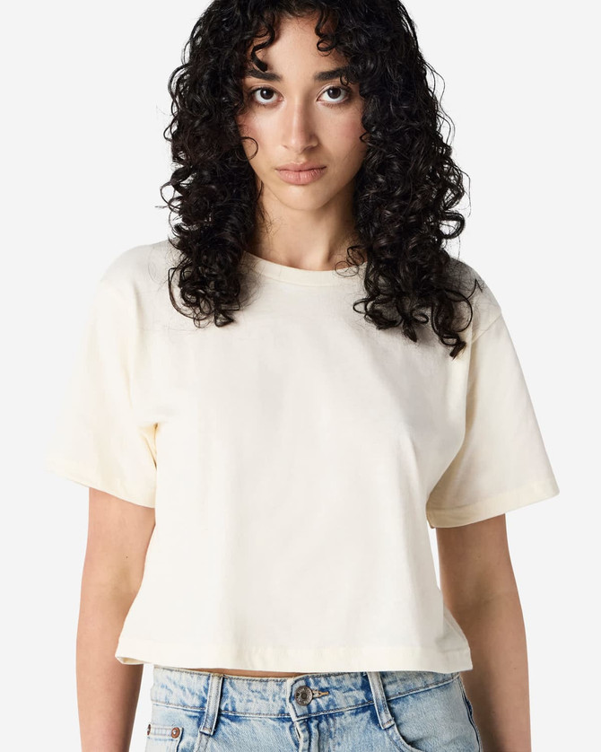 A light cream women's boxy t-shirt displayed on a model, featuring a logo on the garment.