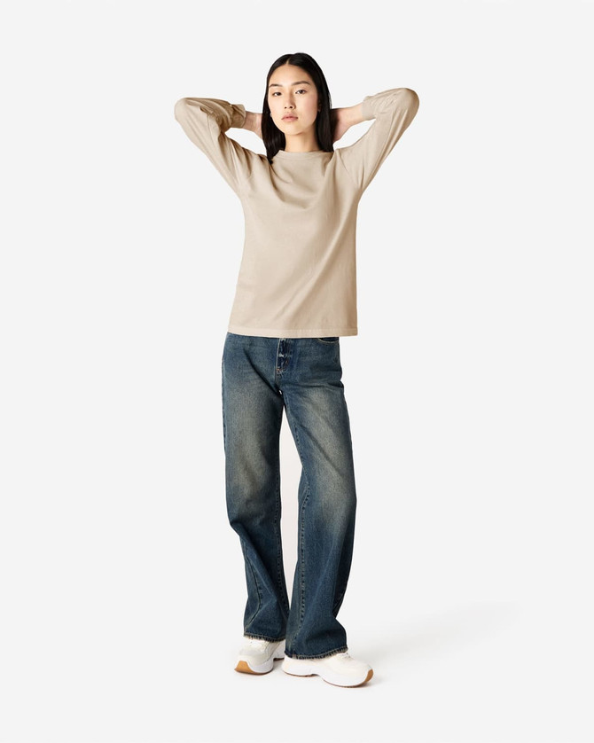 A lightweight long sleeve T-shirt in beige, paired with blue jeans, worn by a model in a casual pose.