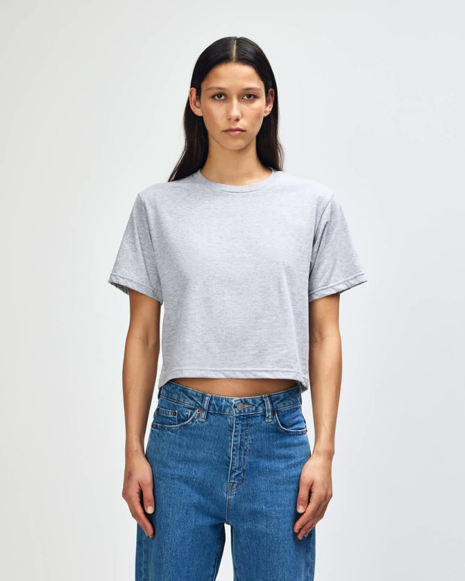 A woman stands wearing a grey boxy T-shirt paired with blue jeans, featuring a logo on the shirt.