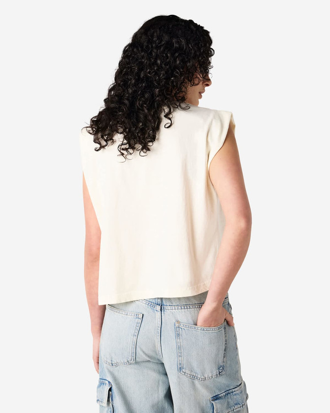 A women's muscle T-shirt in cream, featuring a sleeveless design and a relaxed fit. The shirt has a visible logo.
