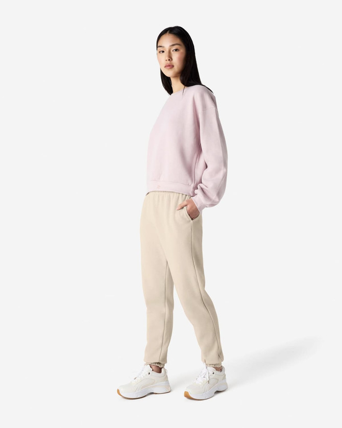 Unisex sweatpants in cream, paired with a pink sweatshirt, worn by a model standing in a neutral background.