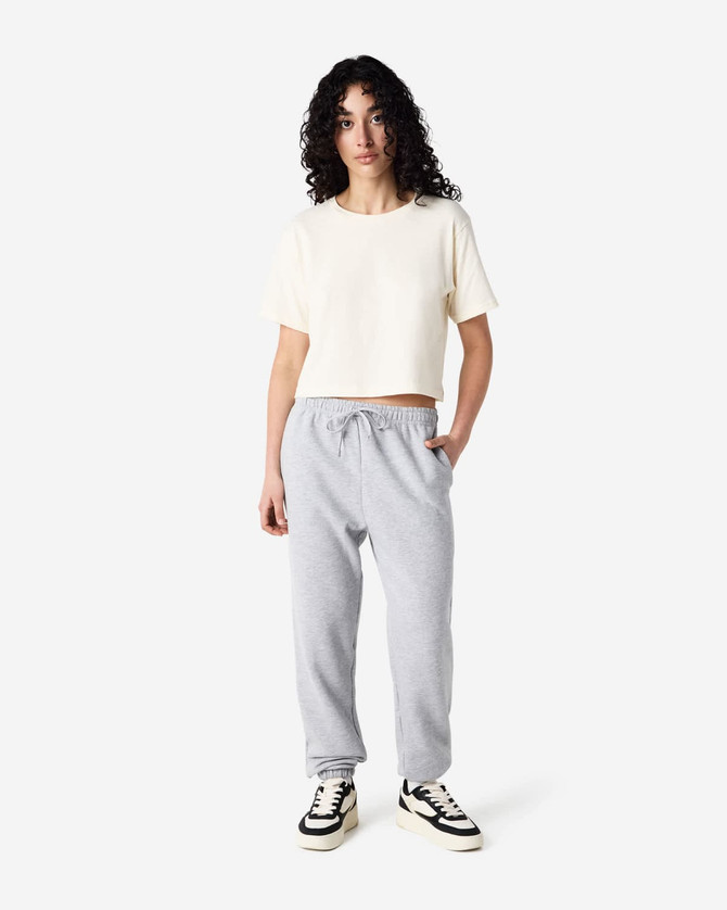 Unisex sweatpants in grey, featured with a cropped cream top, model standing in casual pose, includes branding.