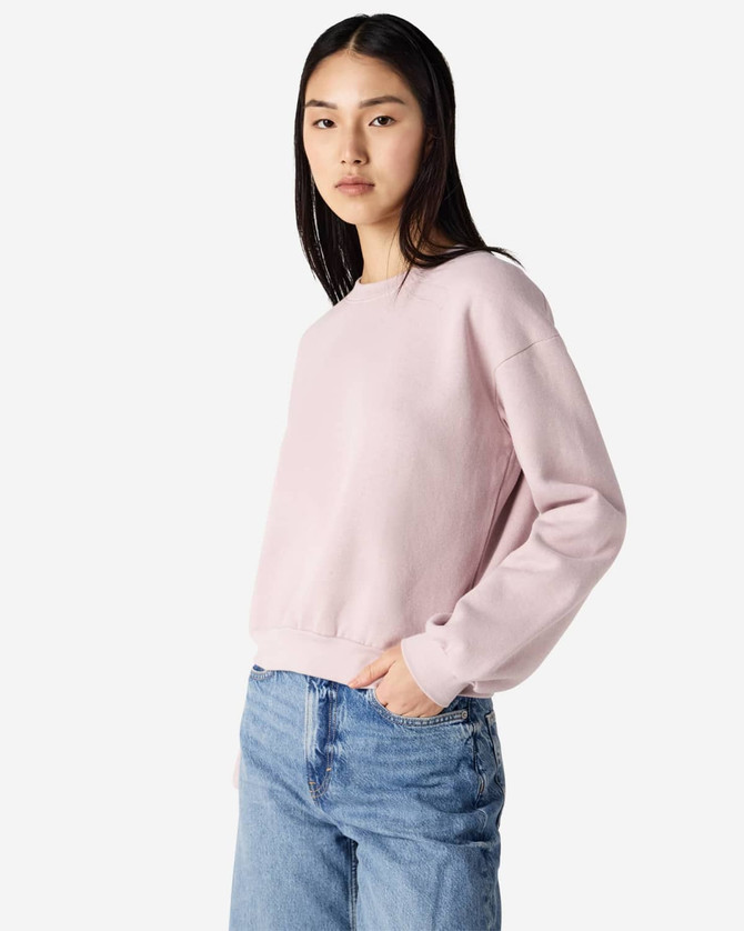 A woman wearing a pink American Apparel Reflex Fleece women's crewneck sweatshirt paired with blue jeans.