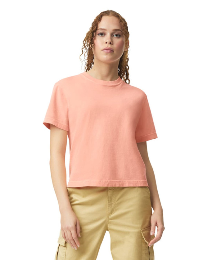 A boxy women's T-shirt in a soft coral colour with short sleeves and a round neckline. It has a logo on it.
