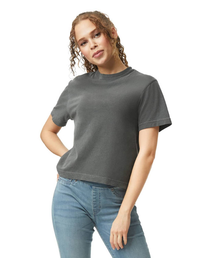 A woman is wearing a dark grey boxy t-shirt paired with blue jeans, with curly hair framing her face.