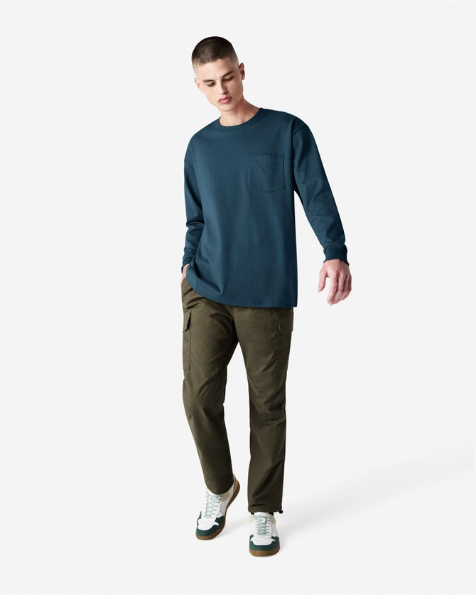 A model wears a navy long-sleeve T-shirt with a pocket, paired with olive green cargo pants and sneakers.