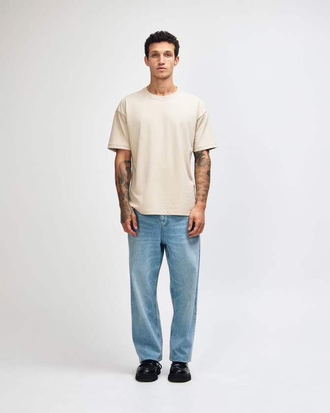 A light beige super heavyweight T-shirt worn by a male model, paired with light blue jeans and sneakers.