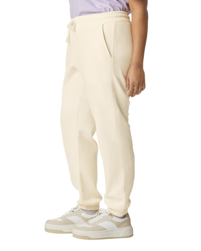 Lightweight cream sweatpants with pockets, featuring a drawstring waist and a logo. Model wears them with sneakers.