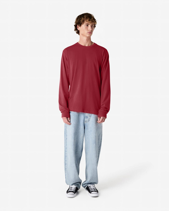 A long sleeve T-shirt in red, paired with light blue baggy jeans and black sneakers, featuring a logo.