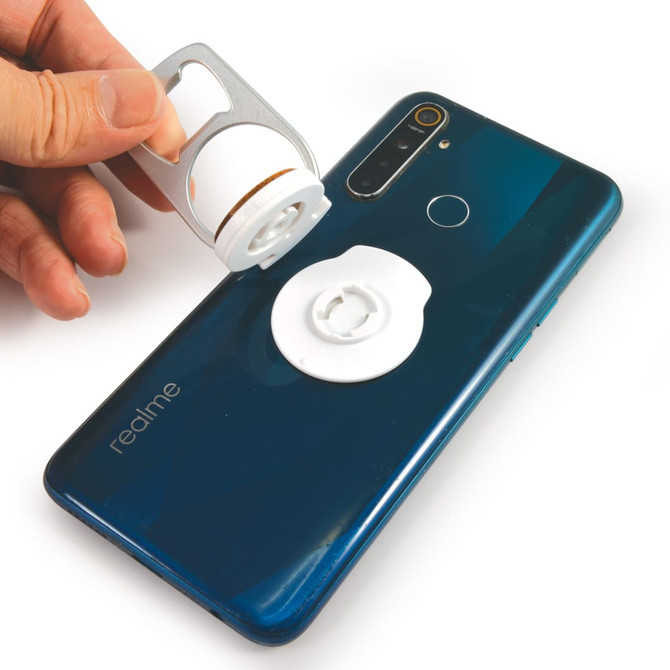 A drink bottle opener in silver being held above a blue smartphone with a white phone stand attached.
