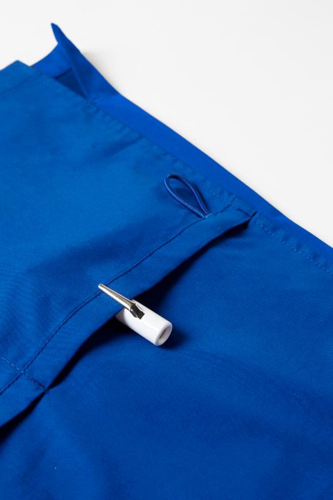 A vibrant blue women's scrub top featuring a pocket with a white toggle. The fabric has a smooth texture.