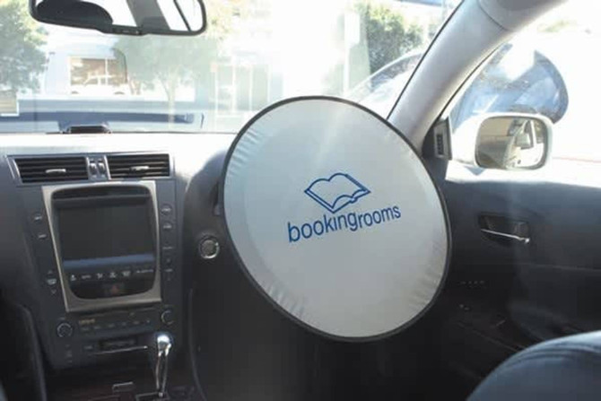 A circular sunshade for a car with a white exterior and a logo, placed on the steering wheel inside a vehicle.