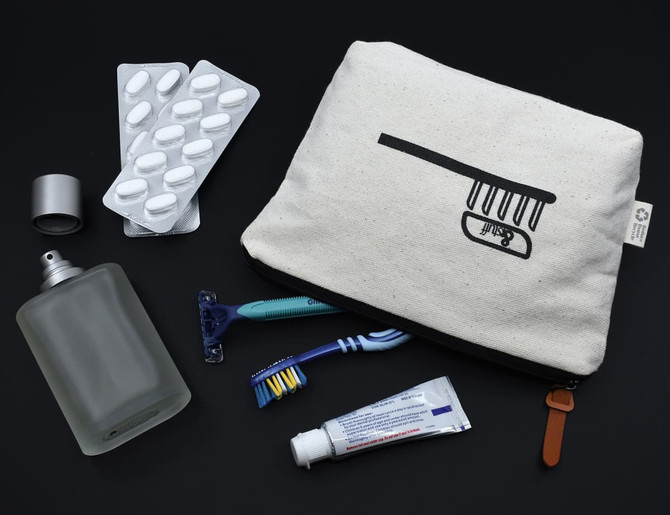 A cream and black toiletry bag with a comb graphic, containing a bottle, razor, toothbrush, and medication strip.