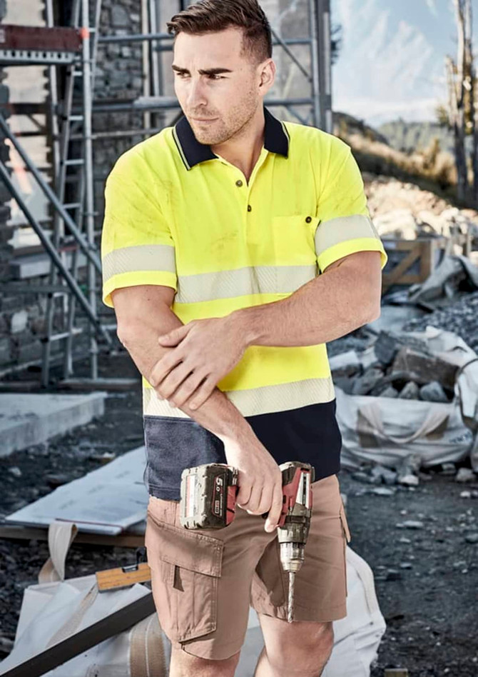 A unisex hi-vis segmented tape short sleeve polo in bright yellow and navy, featuring reflective stripes, held by a man on a worksite.