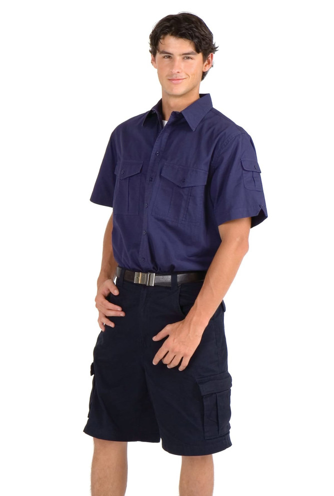 A navy cotton drill short sleeve work shirt with two front pockets, worn by a model paired with dark shorts.