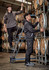 Two men in rugged cooling stretch pants, one standing on a ladder and the other inspecting wooden barrels, in a warehouse setting.
