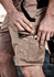Men's streetwear shorts in khaki, featuring multiple pockets and a logo, worn by a man with one hand adjusting a phone.
