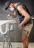 A man wearing a mask and cap works with an air tool, dressed in rugged khaki stretch shorts with a logo.