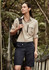 A woman in a light beige shirt and navy shorts stands outdoors, with a backpack over her shoulder. The shorts feature a logo.