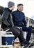 A grey and navy unisex hoodie is worn by two men sitting outdoors, one holding a drink bottle and a cooler nearby.