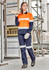A woman in an orange and navy work shirt and matching pants stands on a construction site, holding wooden planks.