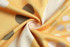 A swirl of fabric featuring yellow and cream with circular patterns in grey and white.