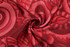 A red patterned fabric featuring intricate swirls and designs, suitable for creating sports uniforms like jerseys.