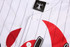 A white baseball uniform with red accents and vertical pinstripes, featuring a logo on the collar.