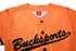 An orange baseball tee with full buttons, featuring black text and a logo on the chest.