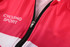 A pink cycling jersey featuring a zipper and a logo, with a lightweight, breathable fabric design.