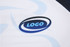 A close-up of a white sports jersey featuring a logo in blue and black. The fabric has a textured pattern.