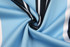 A close-up of fabric in light blue, featuring black and white stripes with a smooth texture. It has a logo.