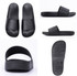 Black slippers featuring a simple design with a flat sole and a wide strap. Contains a logo on the side.