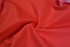 A close-up of smooth, red fabric featuring a twisted texture, showcasing its soft and sleek surface.