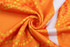 A vibrant orange fabric with yellow and red circular patterns, featuring a smooth, swirling texture.