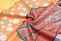 A close-up of a vibrant orange Aboriginal polo shirt fabric featuring intricate patterns and a logo.