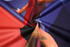 A close-up of a textured fabric featuring vibrant colours, including red, blue, and purple, with a logo present.