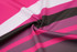 A fabric featuring bold stripes in pink, white, and dark brown colours, showcasing a smooth texture.