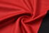 A textured fabric in vibrant red with a black edge, suitable for sports polo shirts. Features a branding logo.