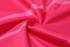 A close-up of a fabric in a vibrant pink colour, featuring a textured pattern. The fabric appears lightweight and smooth.