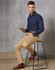 Men's Boston Chino Pants in beige, paired with a navy shirt and brown shoes, displayed on a stool.