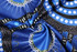 A patterned fabric featuring vibrant blue, black, and white designs, showcasing intricate motifs. The fabric has a smooth texture.