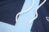 A close-up of a blue tank top hoodie with 3/4 long sleeves and white drawstrings, featuring a logo.