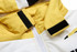 A close-up of a puffer coat featuring yellow and white fabric, with removable sleeves and a hood, and a logo in the design.