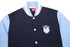 A collegiate jacket featuring navy and light blue colours, with a logo and contrasting striped collar.